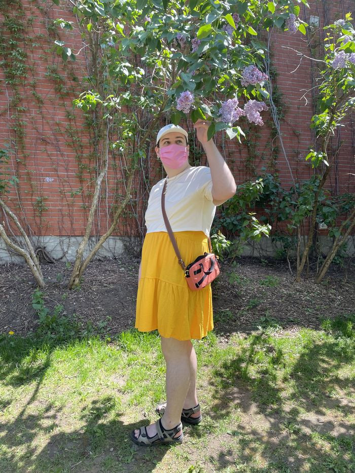 An image with caption: Photo of me wearing a yellow dress, white crop topped tee shirt and pink fabric mask.